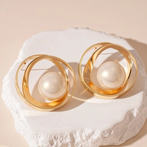 Détail de boucles d'oreilles géométriques dorées avec perle centrale sur socle