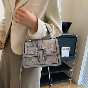 Close-up of grey textured embroidery and silver H-shaped buckle on a square handbag