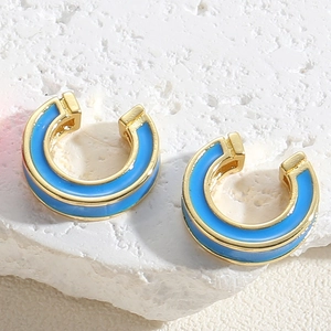 Detail view of gold C-shape earrings with blue enamel inlay on natural stone background