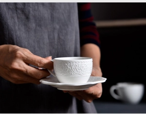 Detailed view of hand holding white porcelain coffee cup with baroque embossed lace texture