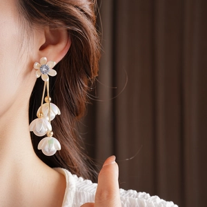 Close-up of gold flower earrings with zircon stone and long pearl tassels on model