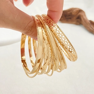 Detail of stacked gold bangles with geometric textures and matte finish on wrist