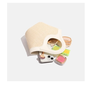 Flat lay of a woven straw handbag with white leather handles and fashion accessories