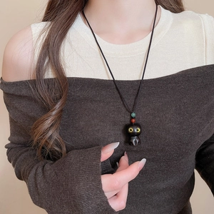Close-up of cute black cat pendant necklace with red and green beads on woven cord