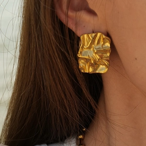 Detailed close-up of a gold pleated irregular geometric stud earring worn on ear