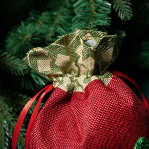 Christmas drawstring gift bag in red and green linen fabric near a festive tree