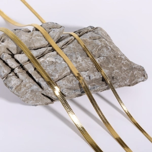 Close-up of golden stainless steel flat snake chains on a natural stone background