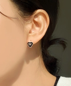 Detail of heart-shaped black enamel earring with gold bow accent worn by a model