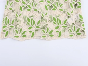 Détail du tissu en dentelle beige avec motifs de feuilles vertes et bords festonnés