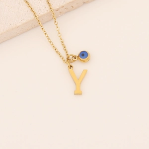 Gros plan du collier pendentif lettre Y doré avec breloque œil bleu sur pierre beige