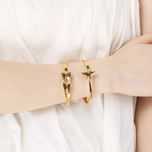 Detail shot of 18K gold plated butterfly and fishtail bangles with zircon inlay on wrist