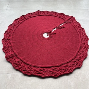 Macro detail of red cable-knit Christmas tree skirt with wavy edges and ribbon ties