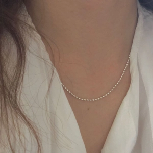Close-up of minimalist S925 silver olive bead necklace on model with white shirt