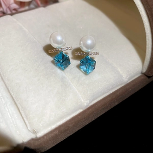 Macro shot of 18k gold plated earrings featuring white pearls and blue hexagonal crystals