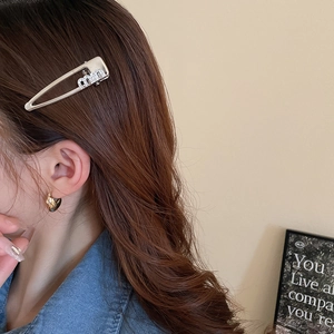 Close-up of a silver Y2K hair clip with rhinestone letters worn on wavy hair