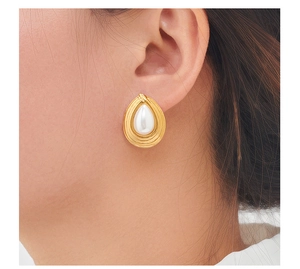 Close-up of teardrop pearl earring with gold textured base worn on an ear
