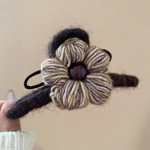 Gros plan d'une pince à cheveux fleur en laine tricotée café et beige avec perle sombre