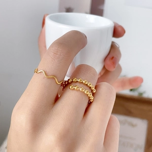 Close-up of minimalist gold wave and bead stackable rings worn by a model
