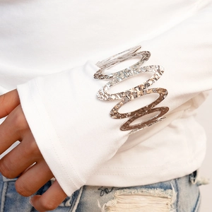 Close-up of hollow oval metal cuff with hammer texture worn over a white shirt sleeve