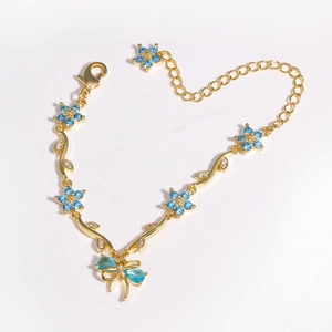 Close-up of golden bracelet with blue zircon flowers and butterfly charm on white background