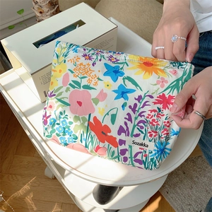 Floral pattern fabric makeup bag with zipper closure held against a white table background
