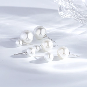 Macro shot of assorted sizes of white round pearl earrings with silver posts on wavy backdrop