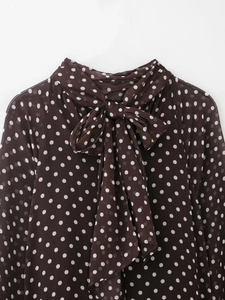 Dettaglio camicia marrone scuro a pois con elegante fiocco grande sullo scollo a V