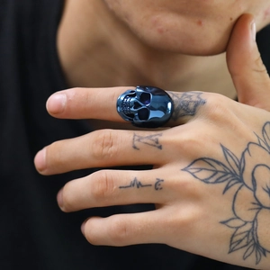 Dettaglio dell'anello a teschio in acciaio blu lucido a specchio su mano tatuata