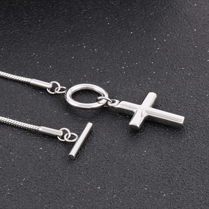 Detail of silver cross pendant with toggle clasp and sleek snake chain on black background