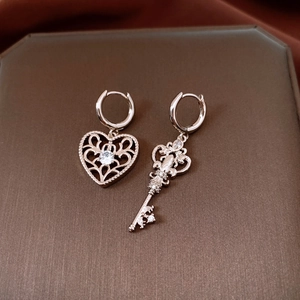 Macro shot of silver heart and key drop earrings with zircons on dark velvet