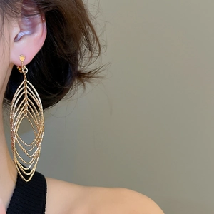 Close-up of layered gold hollow leaf-shaped drop earrings with a textured matte finish