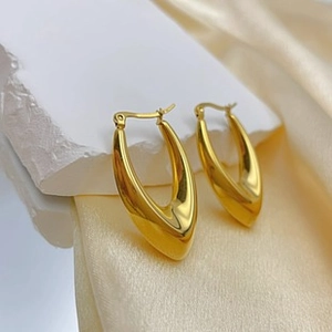 Detail of 18K gold U-shaped earrings on stone pedestal with champagne silk background
