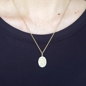 Détail d'un collier tarot ovale doré avec chat et lune peint sur un t-shirt noir élégant
