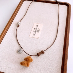Detail of plush puppy pendant with silver heart star and bone bead on brown cord necklace