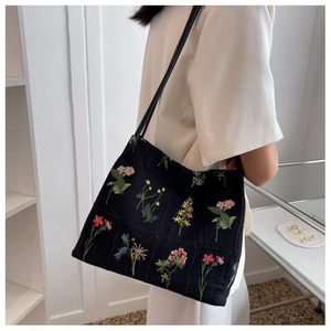 Detail of black knit tote bag featuring colorful floral embroidery and square woven texture