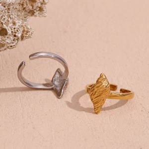 Conch shell inspired 18K gold and silver open rings set on a textured neutral background