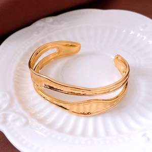 Dettaglio del bracciale dorato a doppio strato ondulato su un vassoio di ceramica bianca