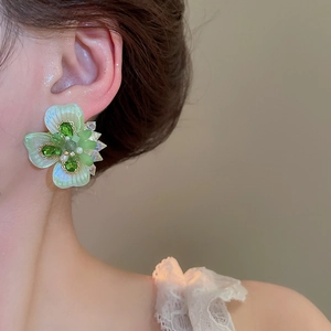 Close-up of flower stud earring with green petals, sparkling crystals and pearl center