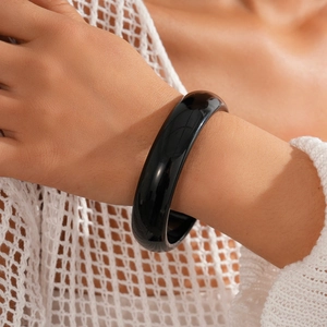 Minimalist wide black resin bangle bracelet styled on a model with white knitwear