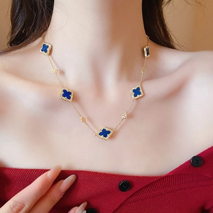 Detail of gold-plated clover necklace with deep blue petals worn on the collarbone