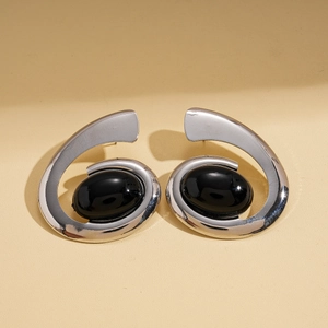 Close-up of silver spiral earrings with oval black gemstones on a beige background