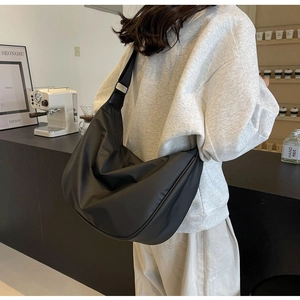 Side view of a large black nylon dumpling crossbody bag worn by a model in a cafe