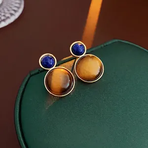 Orecchini vintage tondi in occhio di tigre marrone su un portagioie verde strutturato