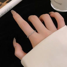 Close-up of a silver wavy band ring worn on a finger for a minimalist layered jewelry look