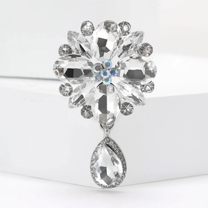 Macro detail of silver flower brooch with clear crystals and water drop pendant on a white stand
