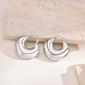 Close-up of polished silver teardrop hoop earrings on a natural stone background