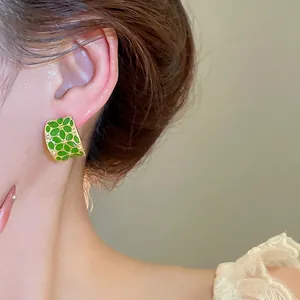 Minimalist C-shaped green enamel flower stud earrings with gold trim on model ear