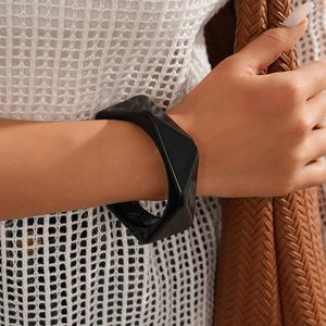Detailed view of a wide black resin geometric bracelet worn by a model in casual attire