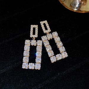 Detailed view of square gold earrings with sparkling crystals on black velvet background