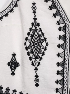 Detailed close-up of contrast diamond embroidery on white cotton-linen fabric surface